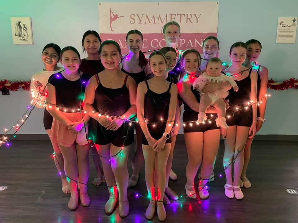 Scranton dance studio Symmetry Dance Company students in ballet outfits posing with Christmas lights and a baby for the holiday dance showcase, highlighting youth ballet and performance opportunities in Scranton 